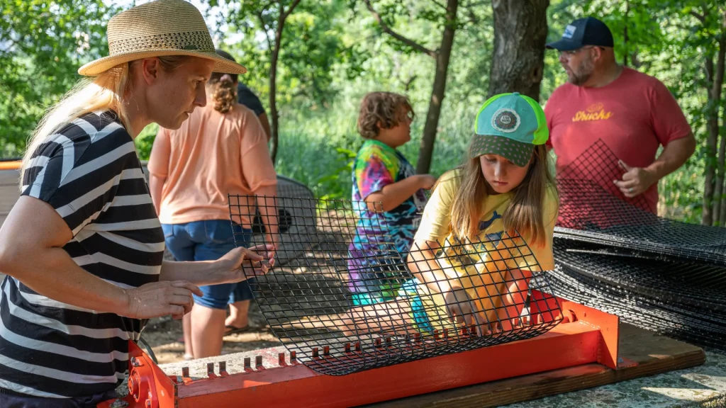 A woman and girl build an oyster cage with more building activity in the background