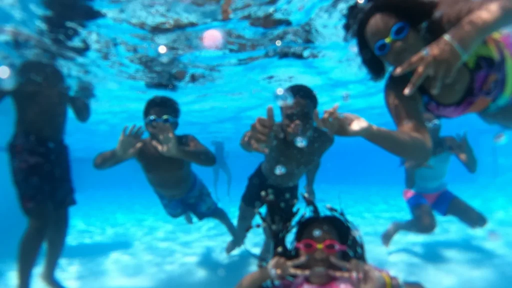 Kids smile and wave at the camera underwater
