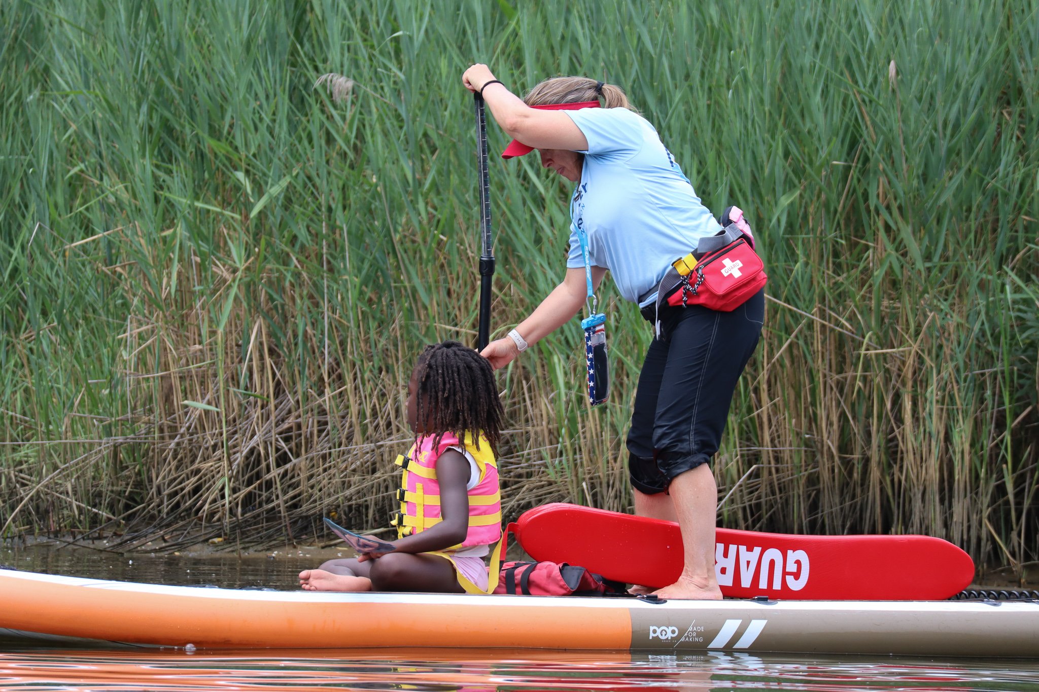 Woman paddles a stand-up board with a child sitting on the front