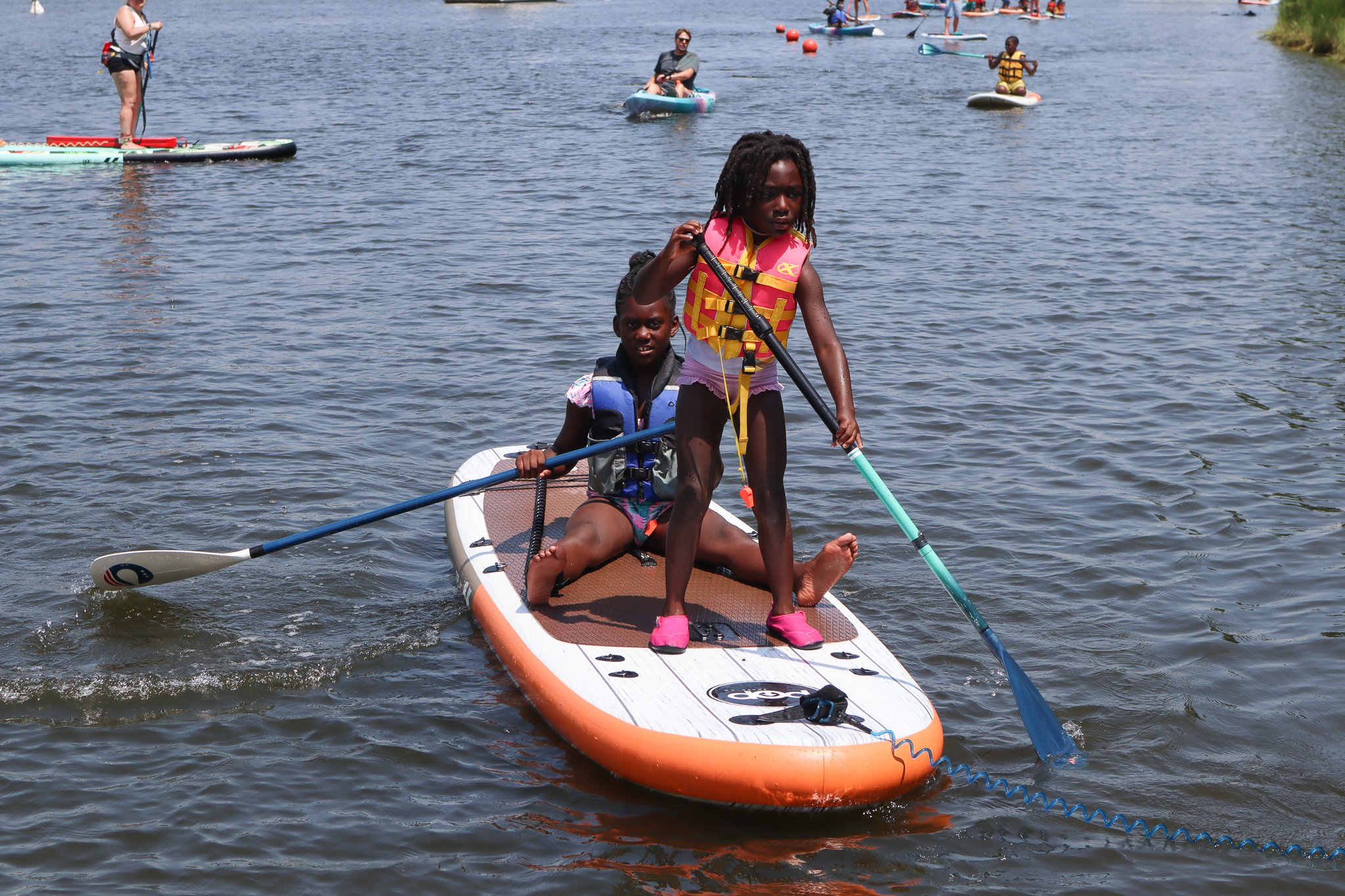 Young girl stand-up paddling with a boy sitting on the back