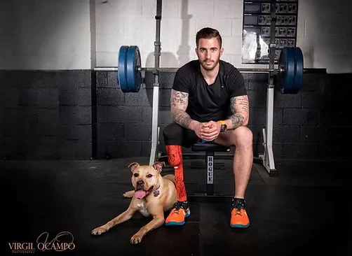 man with leg augmentation sits on a weight bench wit ha dog on the floor by his side