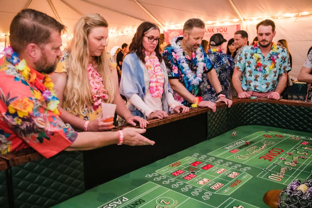 5 people in hawaiian shirts and flower leis stand at a craps table.