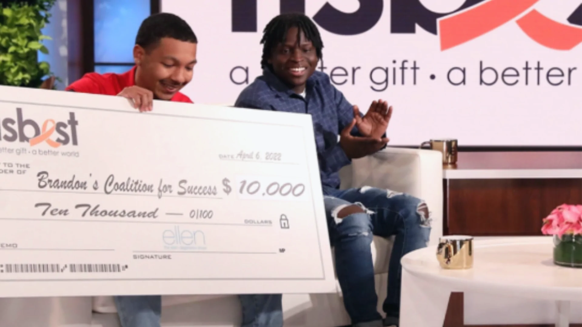 Two men sit on a couch on the Ellen Degeneres show holding an oversized check for $10,000