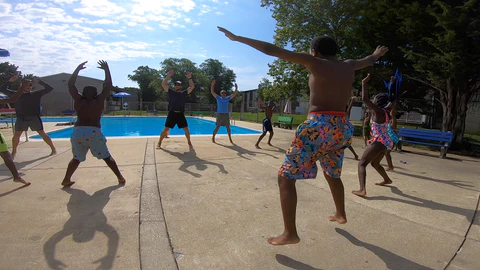 children and a coach exercising by a pool