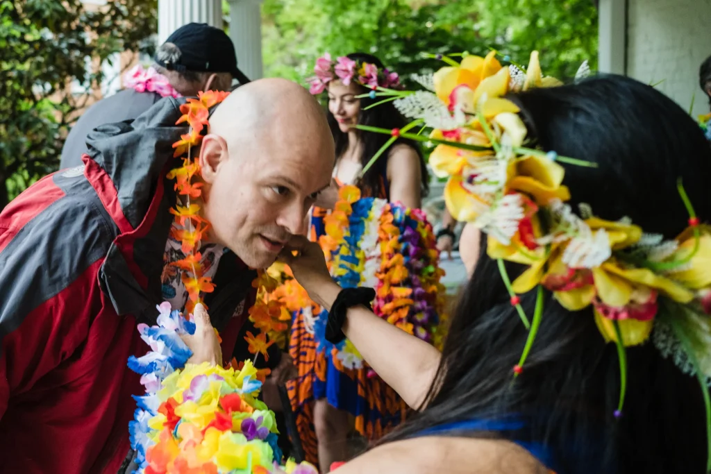 a bald man leans forward as a flower lei is placed around his neck