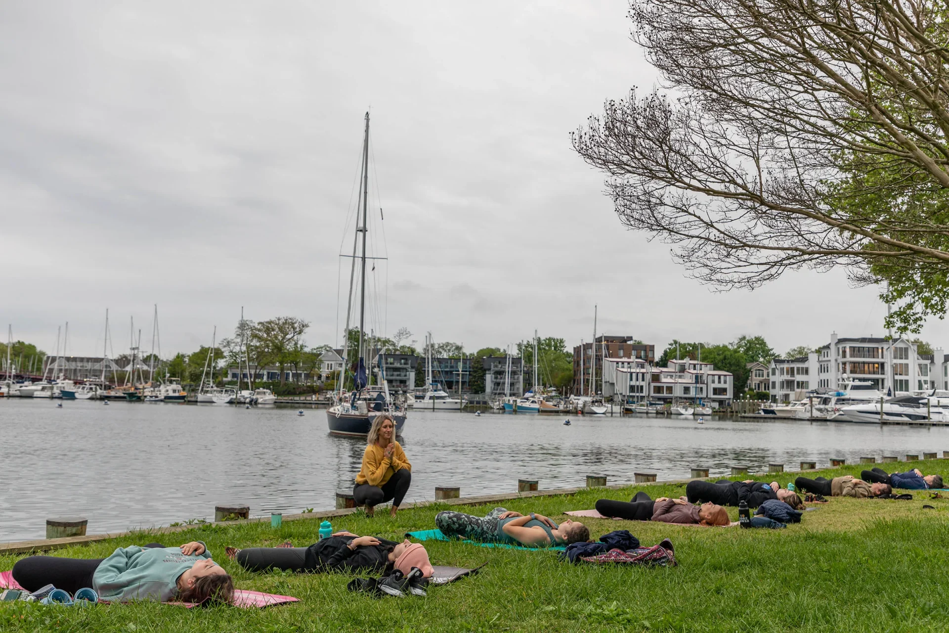 Several people lie on yoga mats in the grass in front of the water.