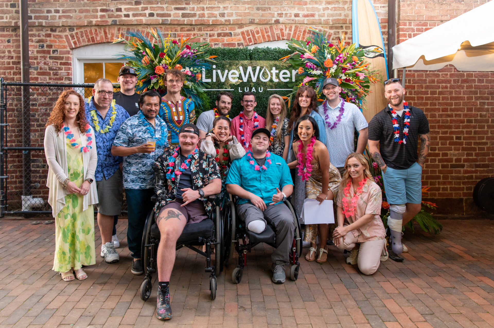 A group of Wounded Warrior participants, including Gaby, pose for a photo in front of a floral backdrop at the Live Water Luau.