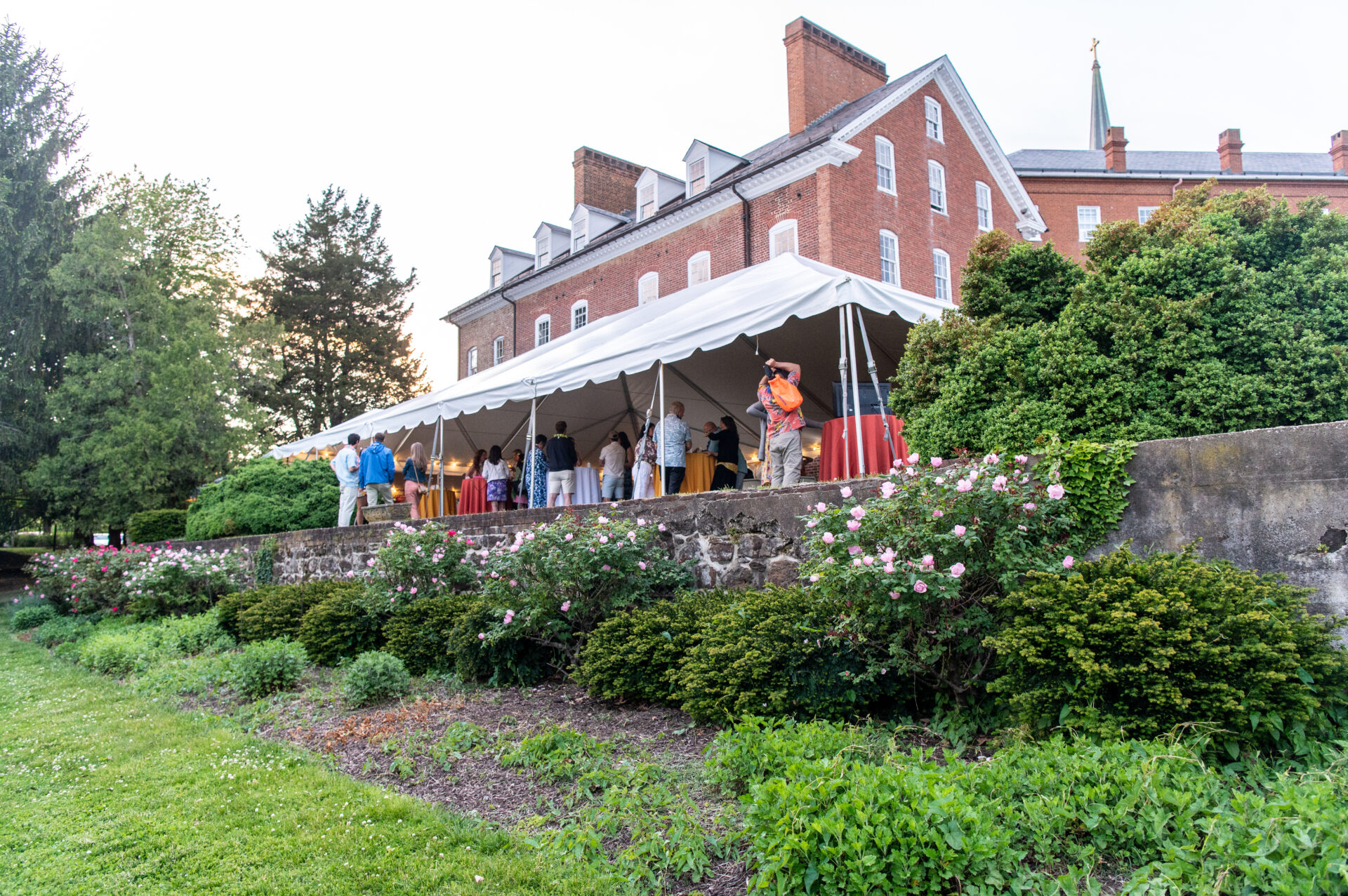 A view of the Charles Carroll House from the garden. A white tent is visible with attendees of the second annual live water luau underneath of it.