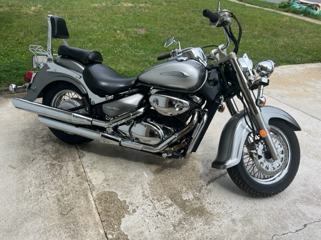 A side angle view of a vintage 2002 Suzuki Volusia Intruder 800 Motorcycle parked on a driveway with some grass visible in the background