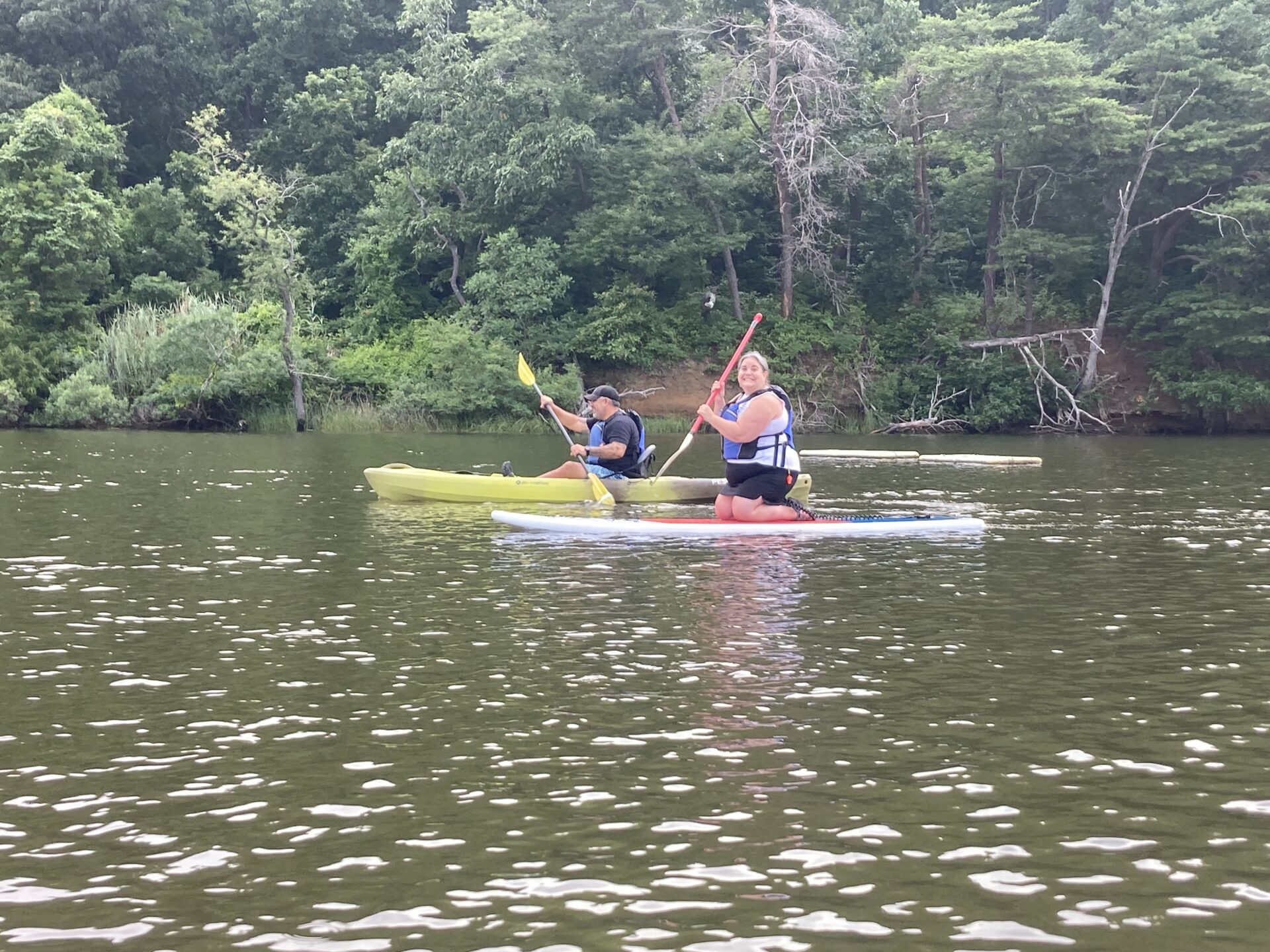 A man and a woman are paddling together on the South River. She is kneeling on a stand up paddle board, and he is sitting in a kayak.